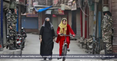 A Kashmir girl rides her bike past Indian security personnel standing guard in front of closed shops in Srinagar, Oct. 30