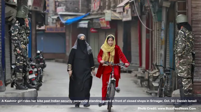 A Kashmir girl rides her bike past Indian security personnel standing guard in front of closed shops in Srinagar, Oct. 30